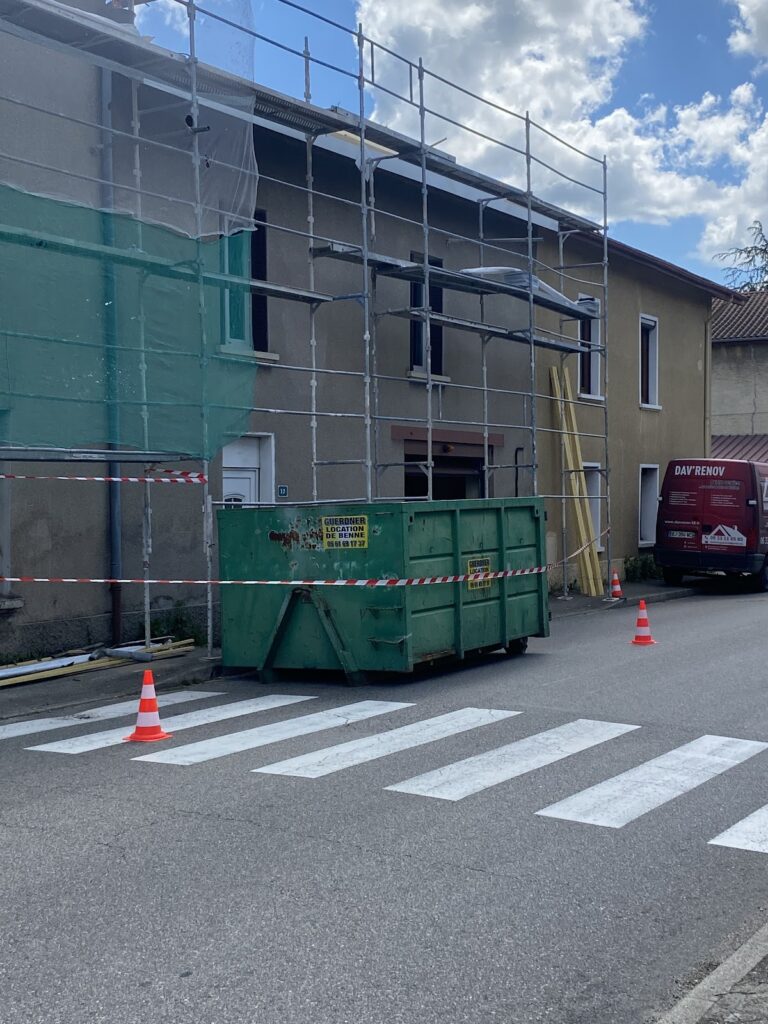 Benne verte Guerdner posée dans la rue devant une façade en travaux, balisée par des cônes, location de benne à Lyon