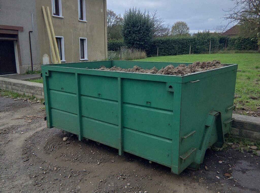 Benne verte remplie de terre et de cailloux au bord d’un jardin en travaux près de Lyon